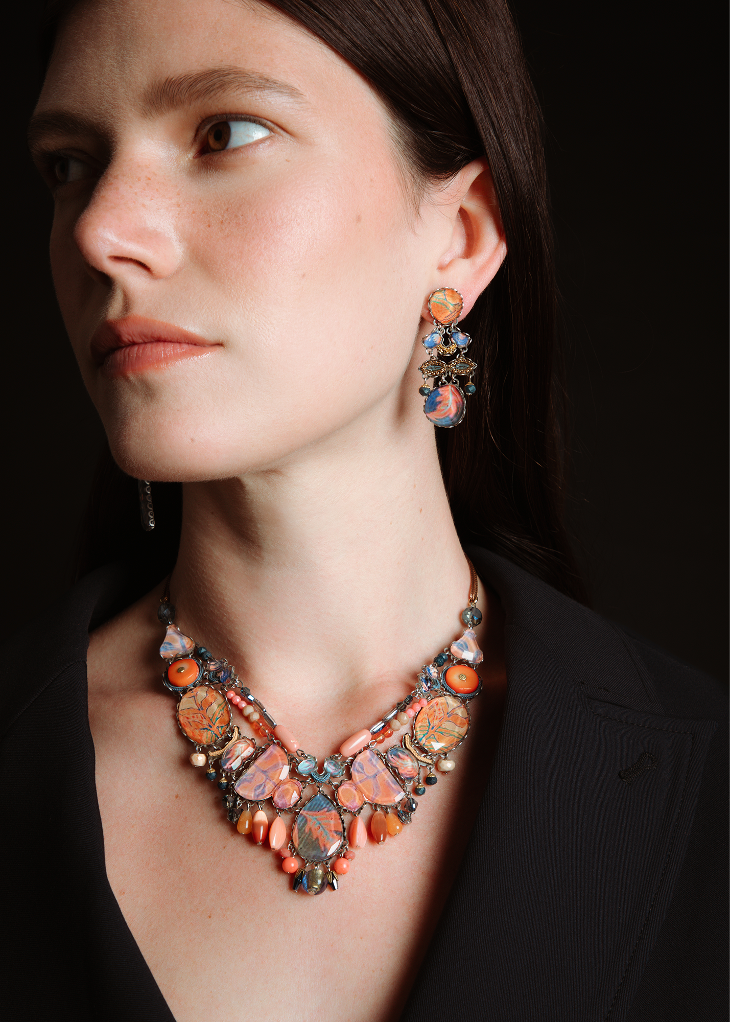 Woman wearing a colorful necklace and earrings against a dark background