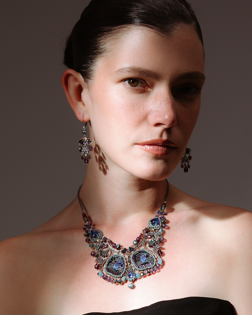 Woman wearing a black strapless dress and colorful necklace with earrings against a dark background