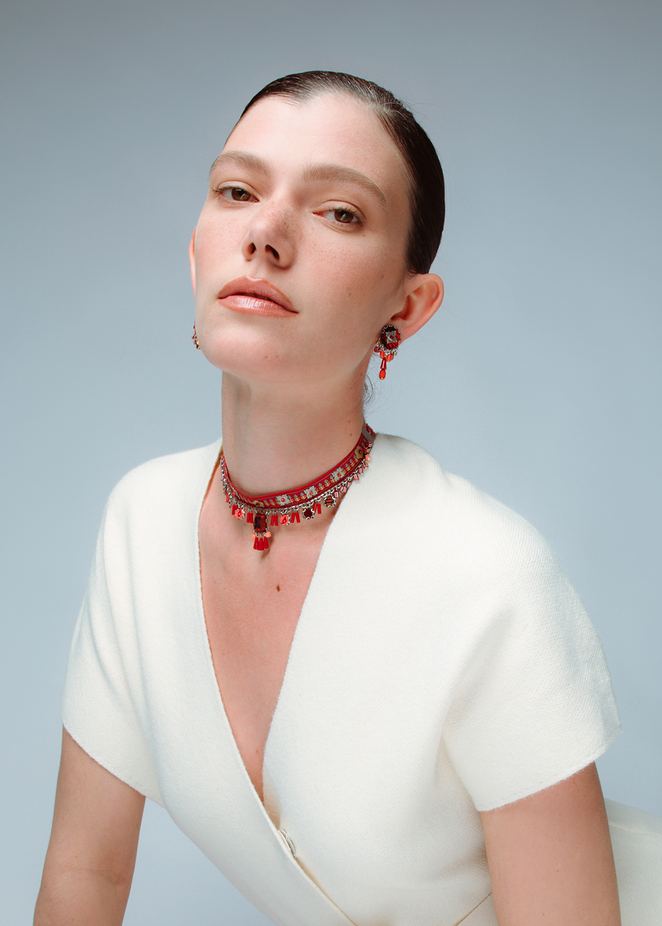 Woman in a white dress with a red necklace against a light gray background